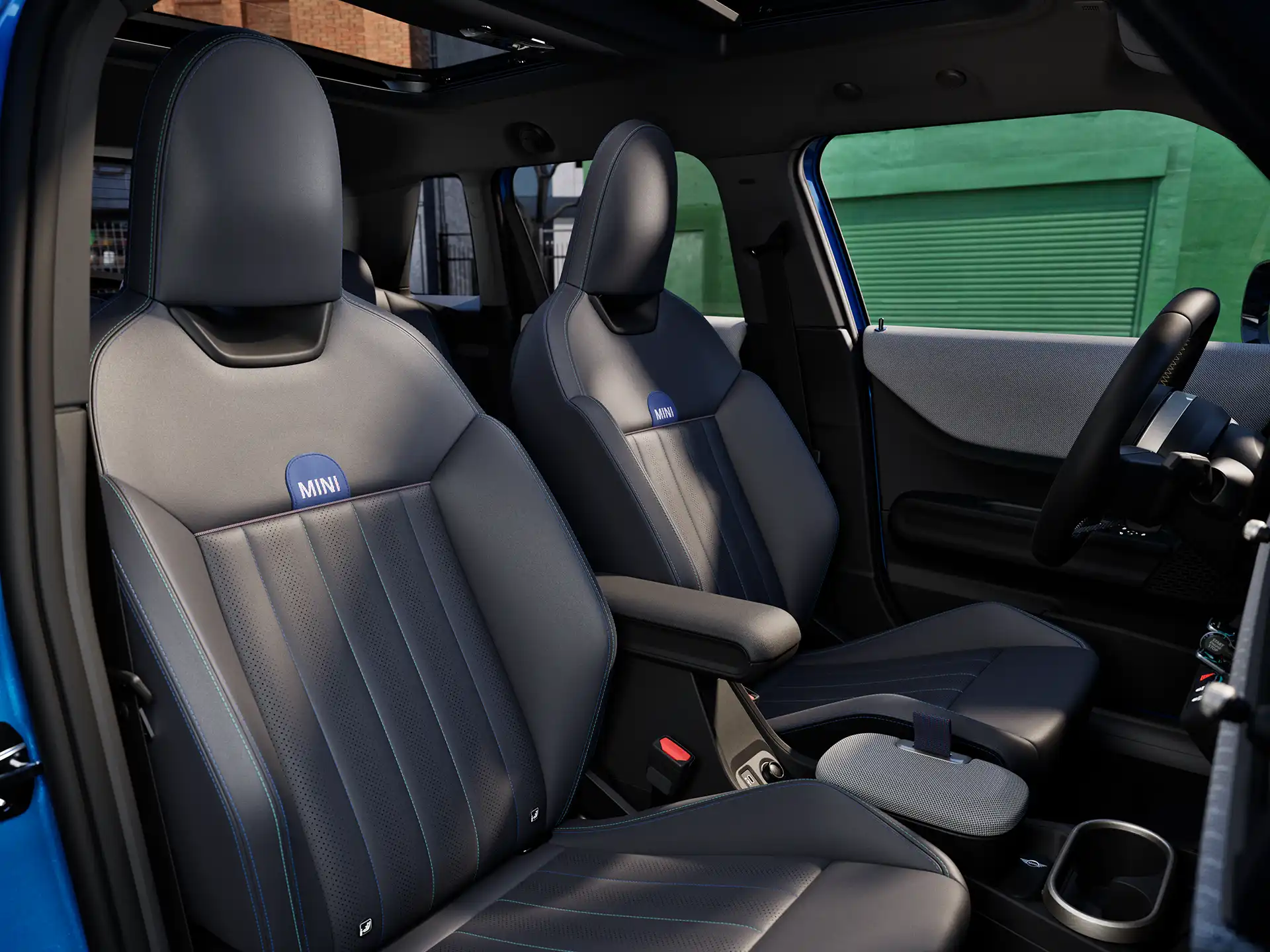 Interior perspective of the MINI Cooper 5-Door is showing the dashboard, steering wheel, round display, panorama glassroof  and back of the frontseats.