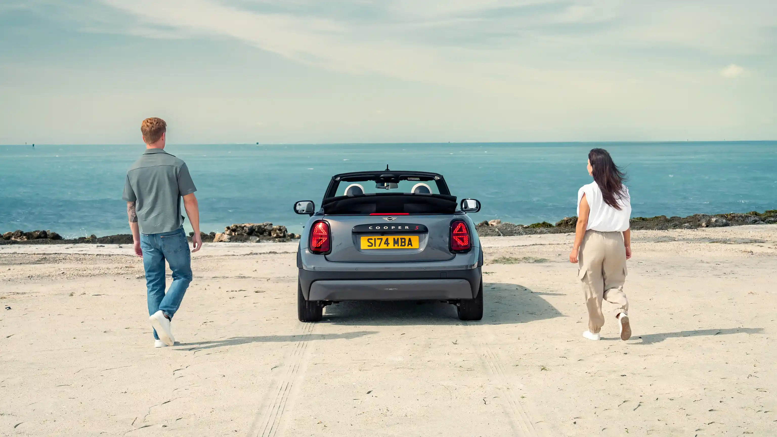 Rear view of a parking MINI Cooper Convertible on a beach with two people