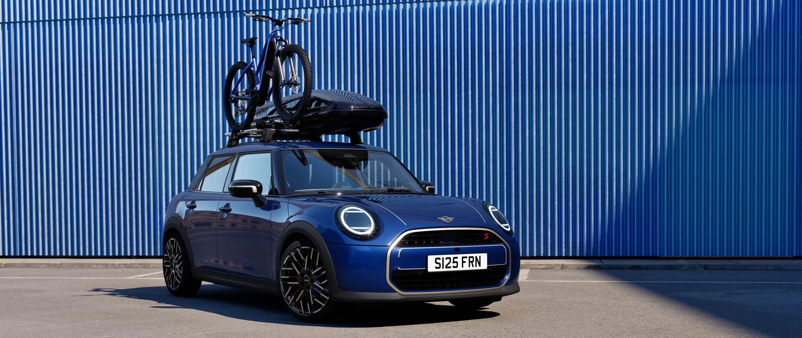 Front view of MINI Aceman in Indigo Sunset Blue with MINI Roof Bike Rack, carrying a mountain bike and MINI Roof Box 320.