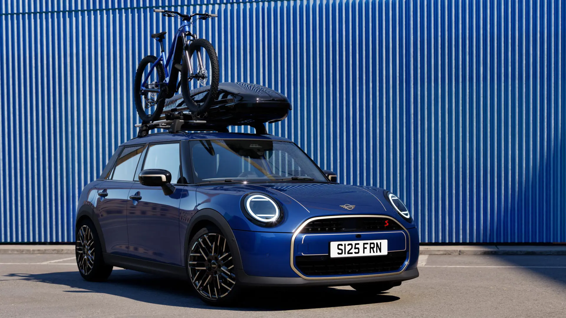 Front view of MINI Aceman in Indigo Sunset Blue with MINI Roof Bike Rack, carrying a mountain bike and MINI Roof Box 320.