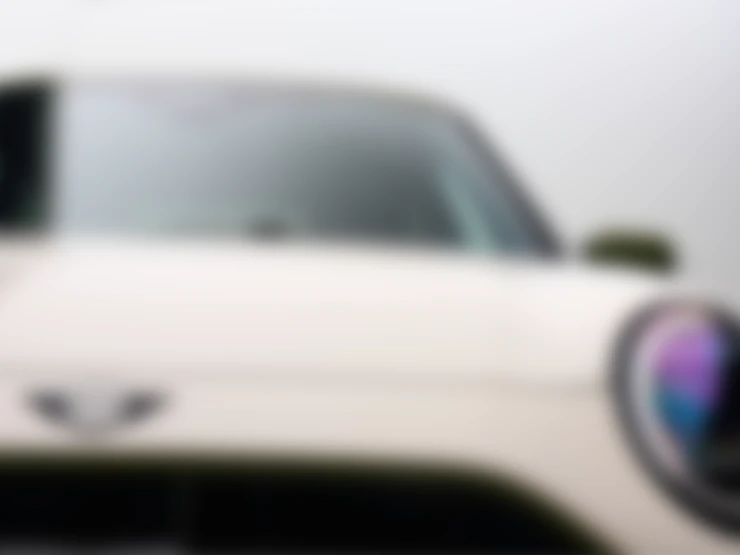 Close front shot of the all-electric MINI Cooper Paul Smith Edition in Inspired White showcasing the headlights and the wing emblem. 