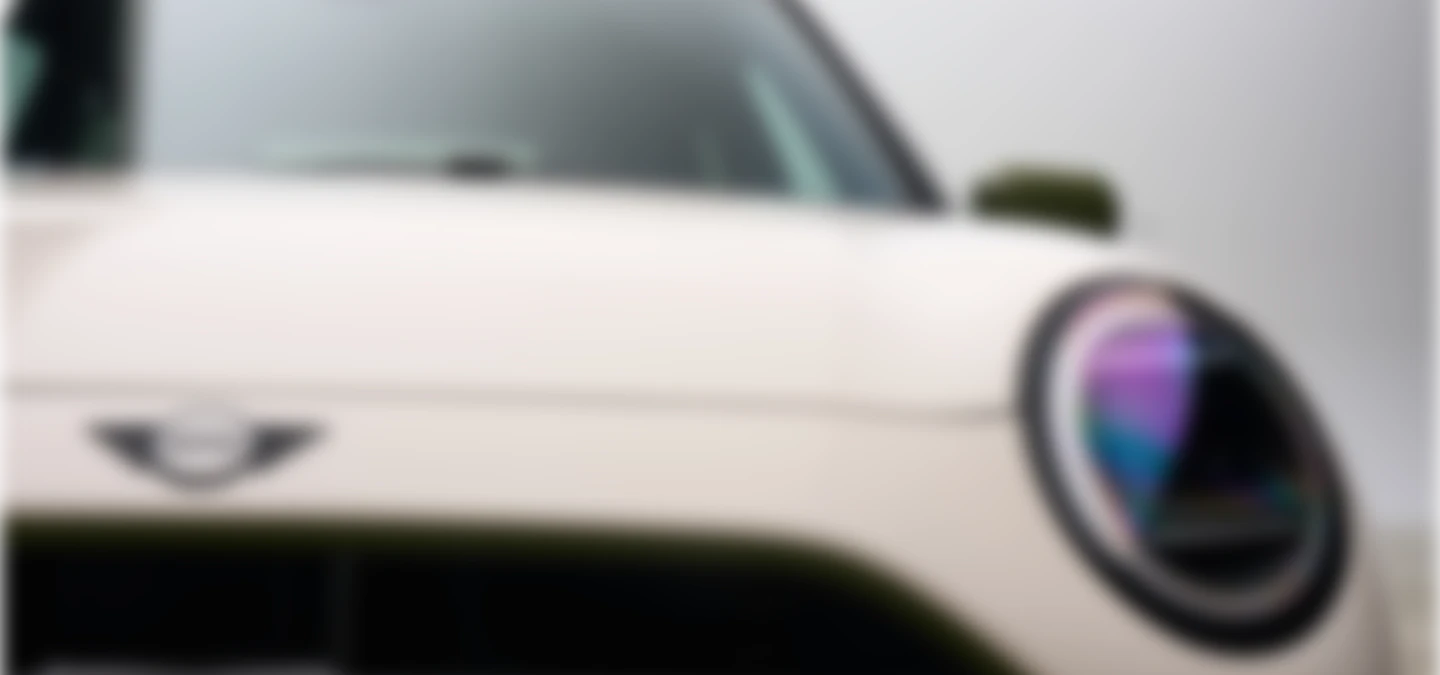 Close front shot of the all-electric MINI Cooper Paul Smith Edition in Inspired White showcasing the headlights and the wing emblem. 