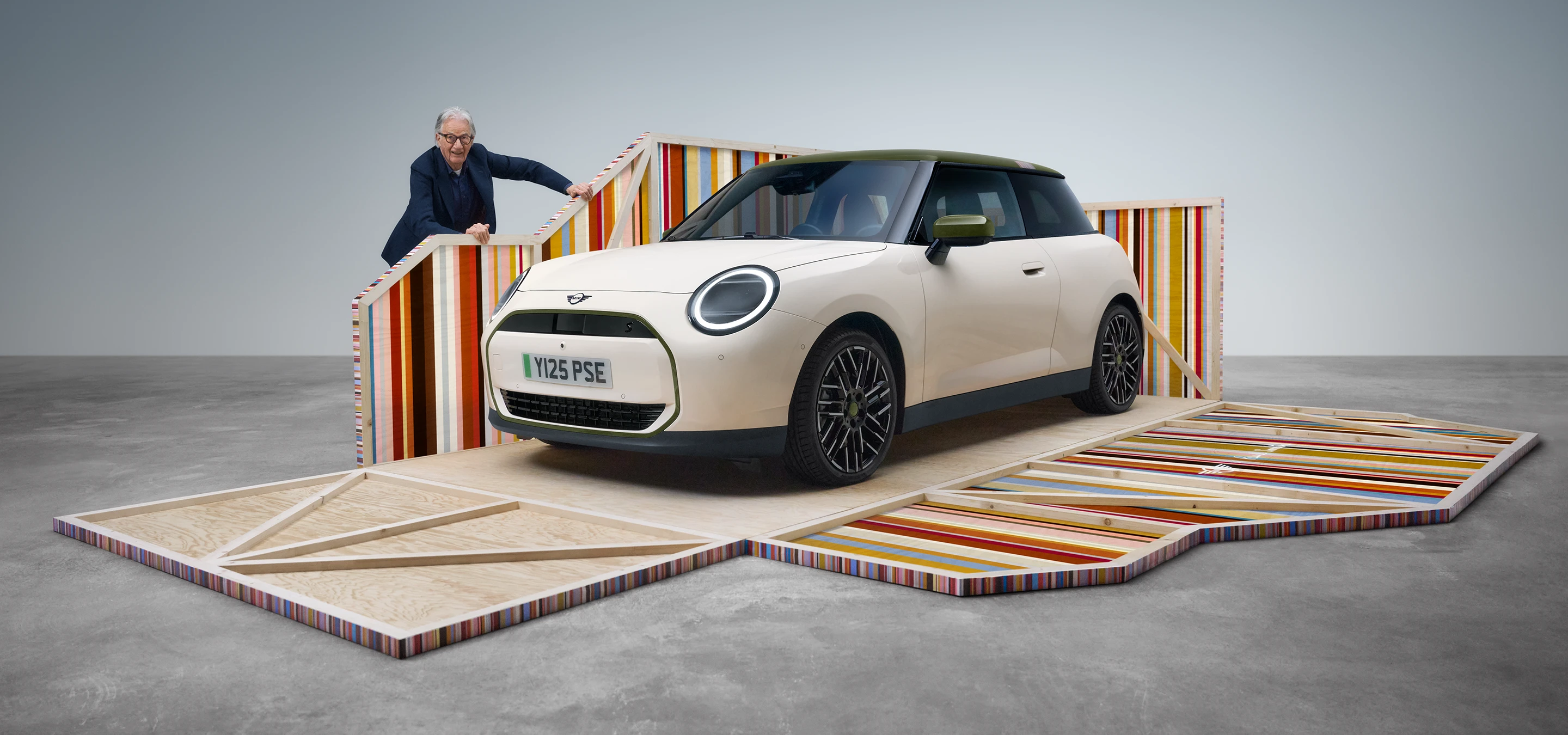 Side view of all-electric MINI Cooper Paul Smith Edition in Inspired White with Paul Smith sitting in the car.